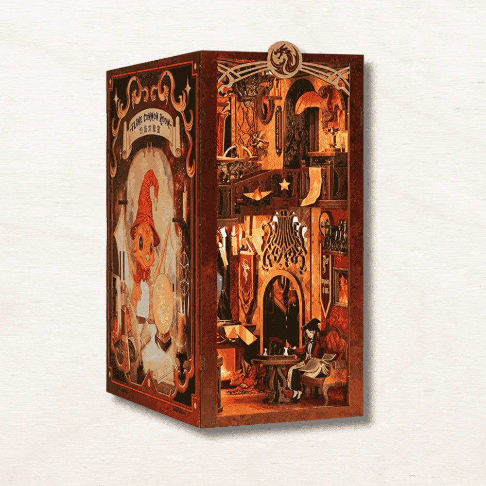 Flame Common Room book nook kit fully assembled and lit between two books, showing a two-floor wizarding common room with glowing LED fireplace and dragon crest